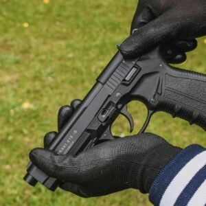 Close-up image showing hands with gloves holding a pistol in a grassy area.